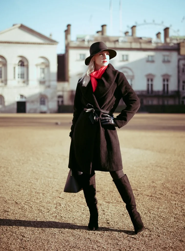 Woman in a dark coat and hat standing in a sunlit London square