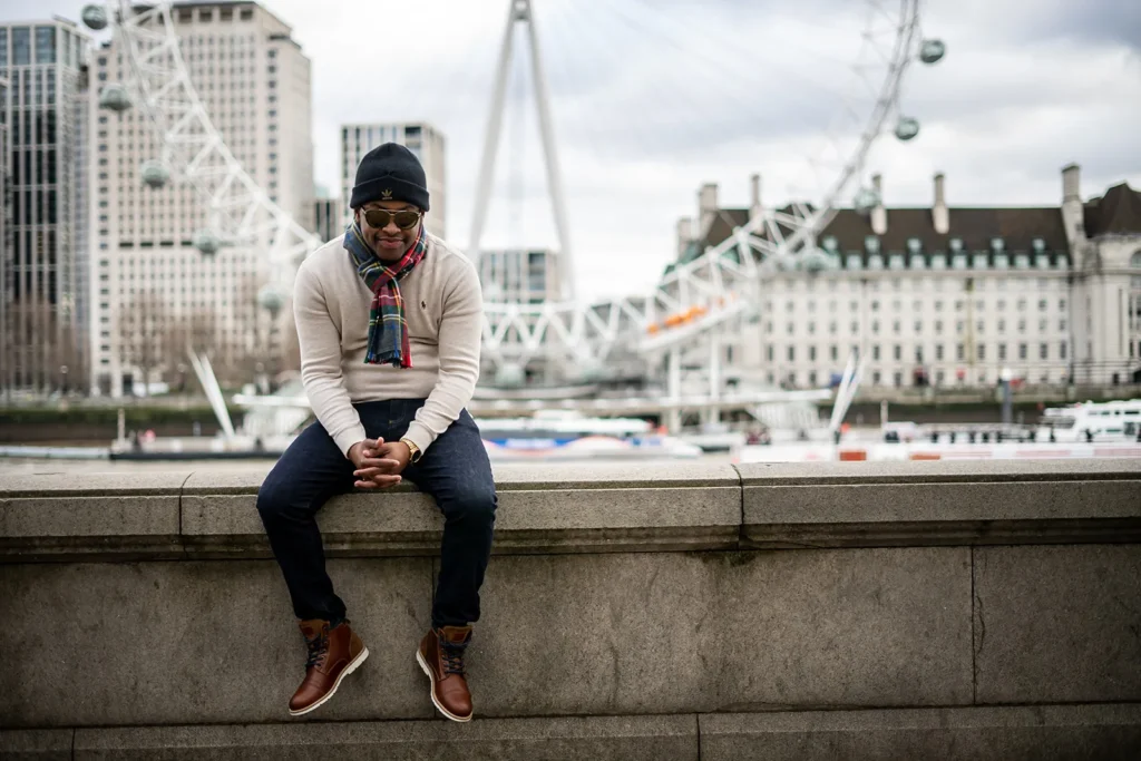 Man seated beside the Thames with the London Eye behind him
