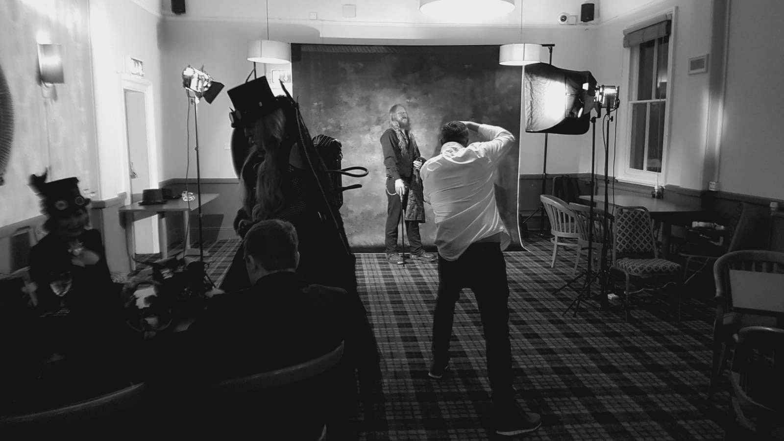 Behind the scenes: the photographer shooting a portrait in front of a painted backdrop, lit by a few lights and a softbox in the upstairs room of a pub